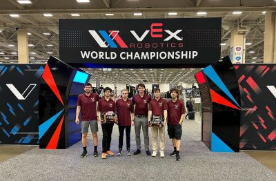 Students standing in front of the VEX World Championship sign with their robots.