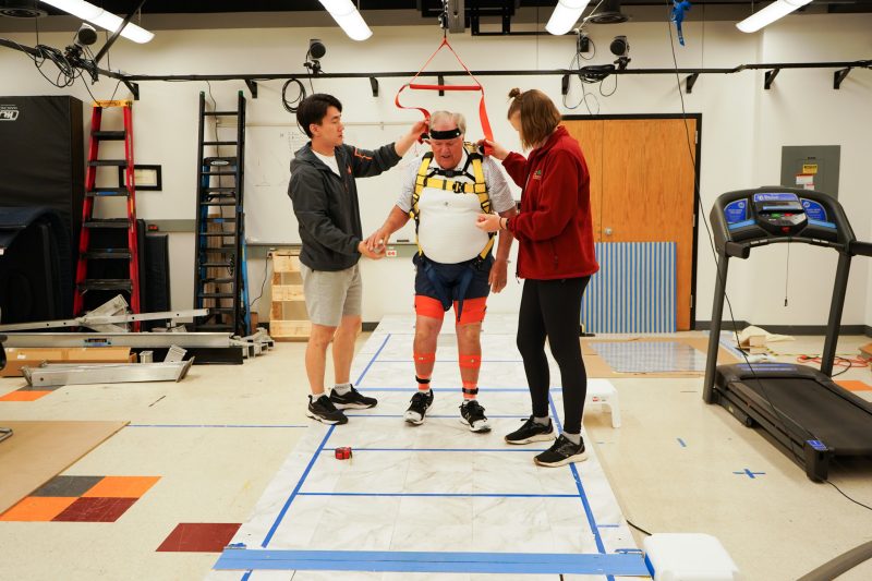 Researchers help a participant in the balance lab get adjusted to his harness